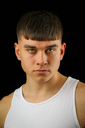 Portrait of a teenage boy in a white sleeveless top against a black backgroundの写真素材