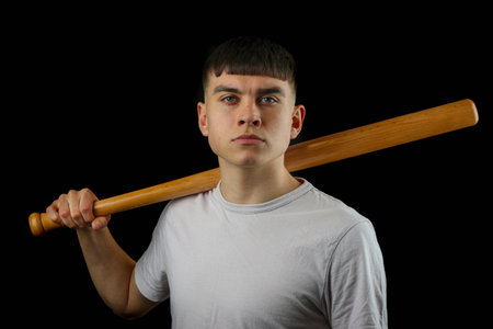A teenage boy with a basball bat against a black background