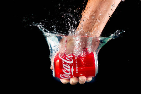 London, United Kingdom, 24th July 2023: A Can of Coca-Cola held in a hand splashing into water against a black backgroundのeditorial素材