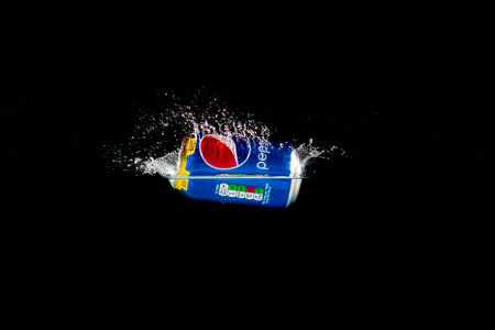 London, United Kingdom, 24th July 2023: A Can of Pepsi splashing into water against a black...