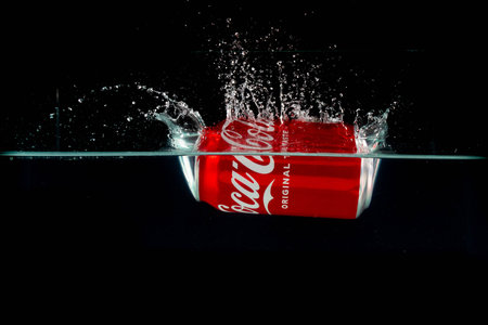 London, United Kingdom, 24th July 2023: A Can of Coca-Cola splashing into water against a black...