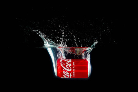 London, United Kingdom, 24th July 2023: A Can of Coca-Cola splashing into water against a black...
