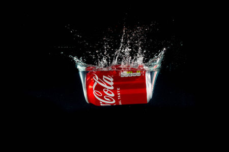London, United Kingdom, 24th July 2023: A Can of Coca-Cola splashing into water against a black...
