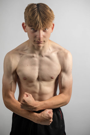 Portrait of a sporty shirtless teenage boy flexing his musclesの写真素材