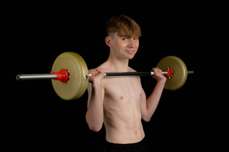 Portrait of a sporty shirtless teenage boy exercising with a barbellの写真素材