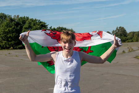 A happy and laughing teenage boy waving the Welsh Flagの写真素材
