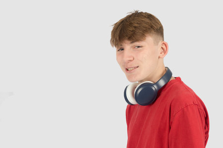 Caucasian 15 year old teenage boy, wearing a red t-shirt,  with headphones loose around his neckの写真素材