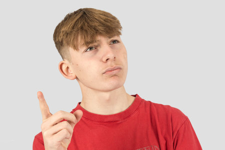A studio portrait of a thinking fifteen year old teenage boy pointing up