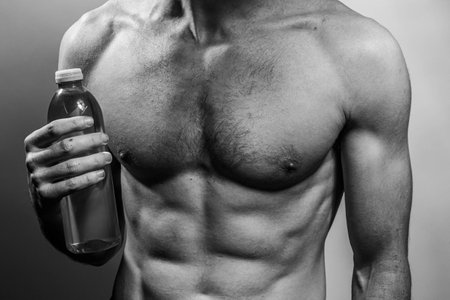A young male body holding a water bottle, with well-defined abs and chest. Model with shirtless torso. Concept of body care, male health, fitness, youth, masculinity, health, weightloss, bodybuildingの写真素材