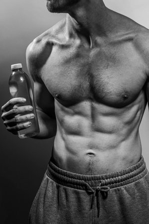 A young male body holding a water bottle, with well-defined abs and chest. Model with shirtless...