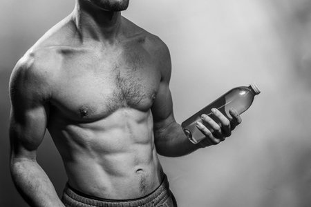 A young male body holding a water bottle, with well-defined abs and chest. Model with shirtless...