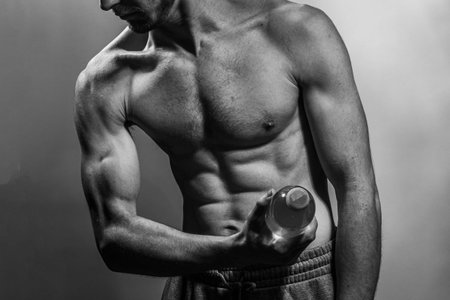 A young male body holding a water bottle, with well-defined abs and chest. Model with shirtless torso. Concept of body care, male health, fitness, youth, masculinity, health, weightloss, bodybuildingの写真素材