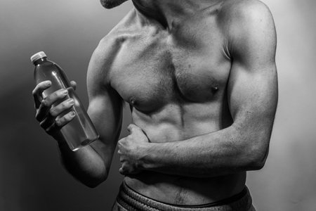 A young male body holding a water bottle, with well-defined abs and chest. Model with shirtless torso. Concept of body care, male health, fitness, youth, masculinity, health, weightloss, bodybuildingの写真素材