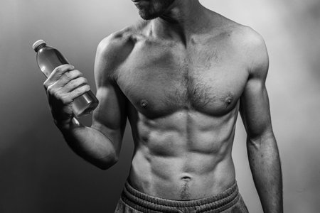 A young male body holding a water bottle, with well-defined abs and chest. Model with shirtless torso. Concept of body care, male health, fitness, youth, masculinity, health, weightloss, bodybuildingの写真素材