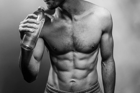 A young male body holding a water bottle, with well-defined abs and chest. Model with shirtless torso. Concept of body care, male health, fitness, youth, masculinity, health, weightloss, bodybuildingの写真素材