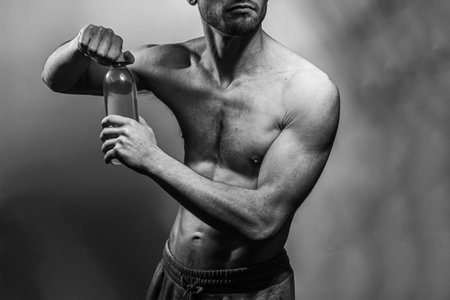 A young male body holding a water bottle, with well-defined abs and chest. Model with shirtless torso. Concept of body care, male health, fitness, youth, masculinity, health, weightloss, bodybuildingの写真素材