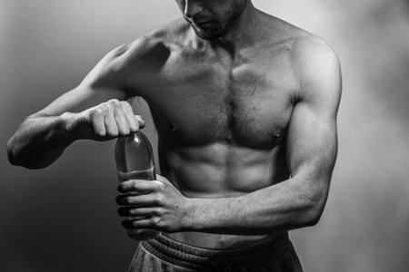 A young male body holding a water bottle, with well-defined abs and chest. Model with shirtless torso. Concept of body care, male health, fitness, youth, masculinity, health, weightloss, bodybuildingの写真素材