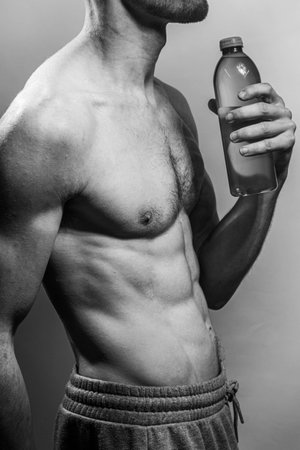 A young male body holding a water bottle, with well-defined abs and chest. Model with shirtless torso. Concept of body care, male health, fitness, youth, masculinity, health, weightloss, bodybuildingの写真素材