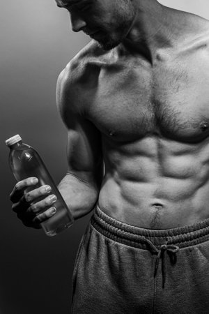 A young male body holding a water bottle, with well-defined abs and chest. Model with shirtless torso. Concept of body care, male health, fitness, youth, masculinity, health, weightloss, bodybuildingの写真素材