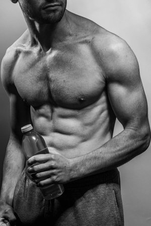 A young male body holding a water bottle, with well-defined abs and chest. Model with shirtless torso. Concept of body care, male health, fitness, youth, masculinity, health, weightloss, bodybuildingの写真素材
