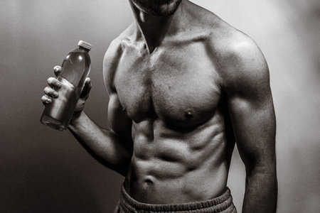 A young male body holding a water bottle, with well-defined abs and chest. Model with shirtless torso. Concept of body care, male health, fitness, youth, masculinity, health, weightloss, bodybuildingの写真素材