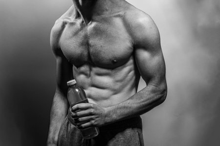 A young male body holding a water bottle, with well-defined abs and chest. Model with shirtless torso. Concept of body care, male health, fitness, youth, masculinity, health, weightloss, bodybuildingの写真素材