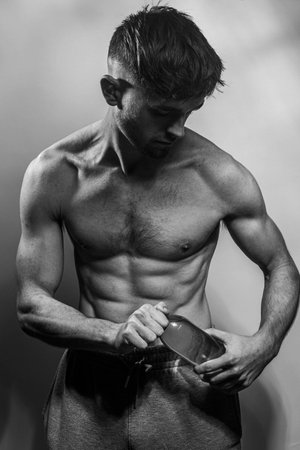 A young male body holding a water bottle, with well-defined abs and chest. Model with shirtless torso. Concept of body care, male health, fitness, youth, masculinity, health, weightloss, bodybuildingの写真素材