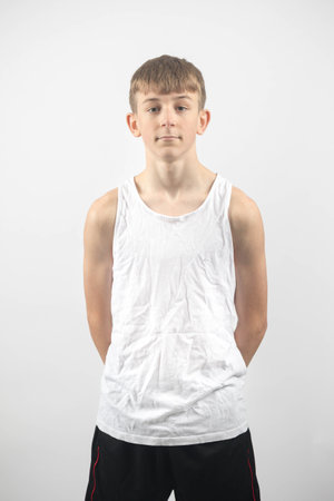 Fifteen year old teenage boy wearing a sleeveless top, studio shot against a white background