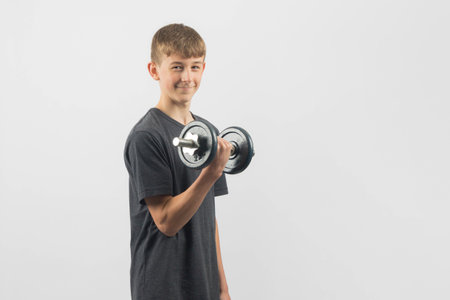 Fifteen year old teenage boy exercising with dumbbells, studio shot against a white backgroundの写真素材