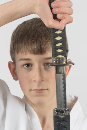 Fifteen year old male teenage karate black belt drawing a katana, studio shot against a white backgroundの写真素材