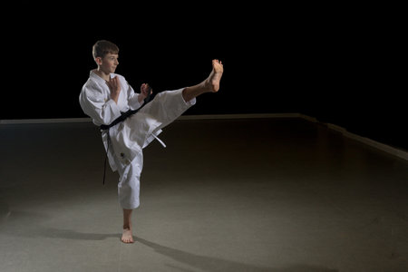 Fifteen year old male teenage karate black belt doing a front kick, studio shot against a black backgroundの写真素材