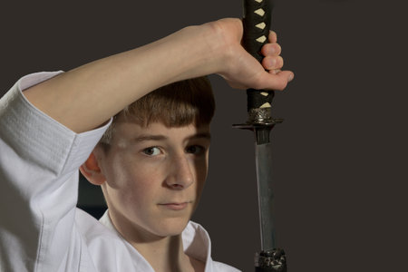 Fifteen year old male teenage karate black belt drawing a sword, studio shot against a black backgroundの写真素材