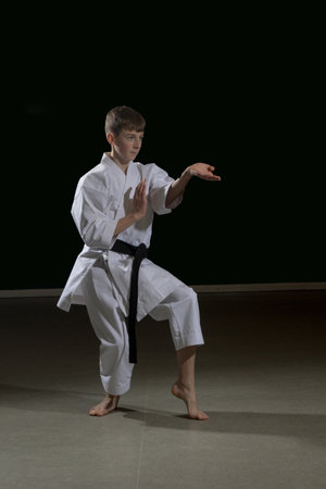 Fifteen year old male teenage karate black belt performing kata Kururunfa, studio shot against a black backgroundの写真素材