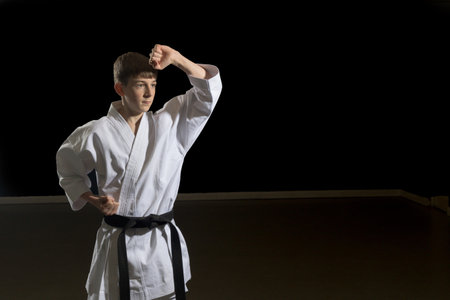 Fifteen year old male teenage karate black belt doing a body block, studio shot against a black backgroundの写真素材