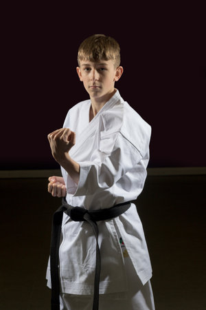 Fifteen year old male teenage karate black belt perfoming a block, studio shot against a black backgroundの写真素材