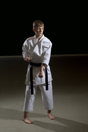 Fifteen year old male teenage karate black belt doing a block, studio shot against a black backgroundの写真素材