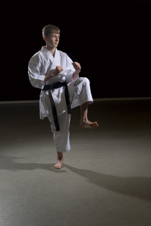 Fifteen year old male teenage karate black belt kicking, studio shot against a black backgroundの写真素材