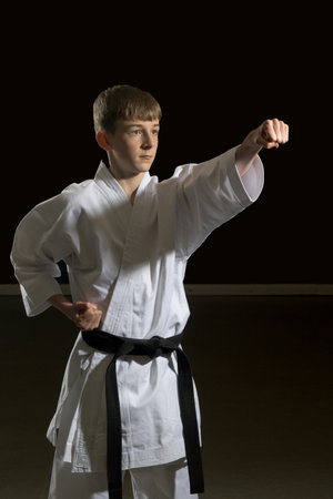 Fifteen year old male teenage karate black belt punching, studio shot against a black backgroundの写真素材