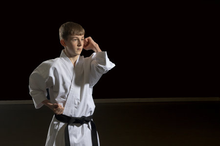 Fifteen year old male teenage karate black belt doing an elbow strike, studio shot against a black backgroundの写真素材
