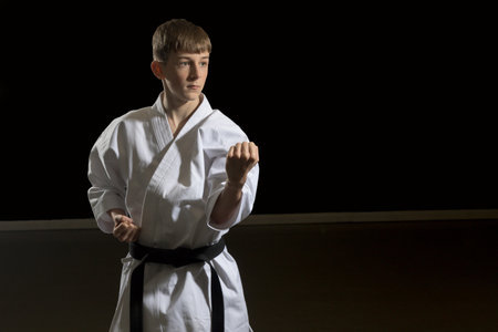 Fifteen year old male teenage karate black belt doing a body block, studio shot against a black backgroundの写真素材