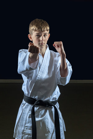 Fifteen year old male teenage karate black belt attacking, studio shot against a black background