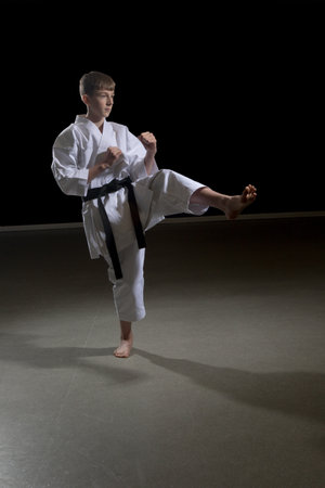 Fifteen year old male teenage karate black belt kicking, studio shot against a black backgroundの写真素材