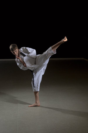 Fifteen year old male teenage karate black belt doing a side kick, studio shot against a black backgroundの写真素材