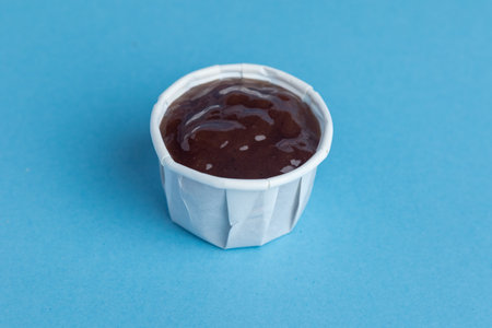 A Paper Container Filled With Sauce. Studio Shot Against A Blue Backgroundの写真素材
