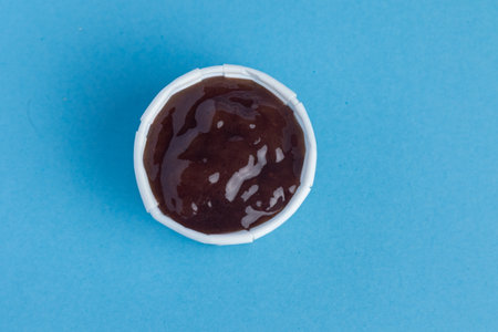 A Paper Container Filled With Sauce. Studio Shot Against A Blue Backgroundの写真素材