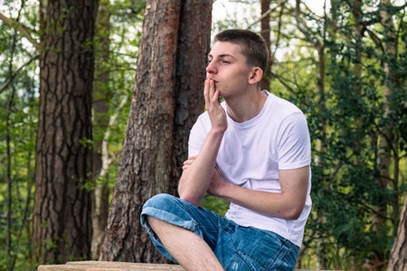 Thinking Teenage boy sitting on a bench in a public park, wearing a white t-shirt and blue denimの写真素材