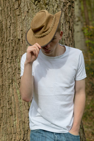 Teenage boy wearing a hat, white t-shirt and blue denim. On hand is on the hat, pulling it downの写真素材