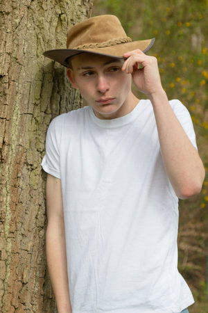 Teenage boy wearing a hat, white t-shirt and blue denim. One hand is on the hatの写真素材