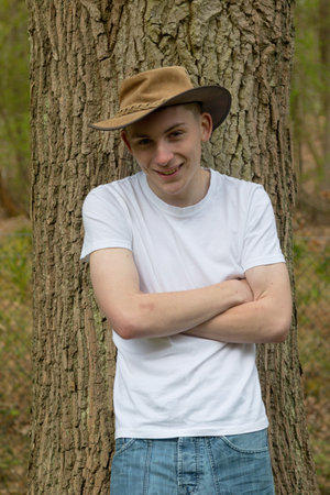 Happy and smiling teenage boy wearing a bush hat, white t-shirt and blue denim. With folded arms.の写真素材