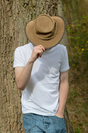Teenage boy wearing a bush hat, white t-shirt and blue denim. On hand is on the hat, pulling it downの写真素材